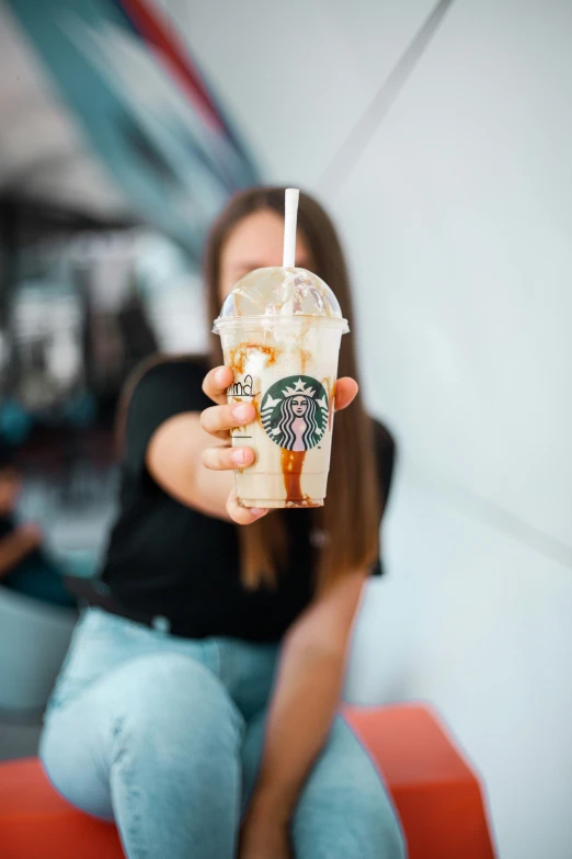 a young lady sitting down holding up a starbucks drink