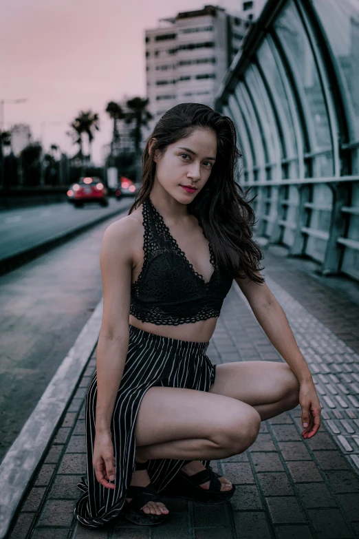 a young woman squatting in the street with the cityscape behind her