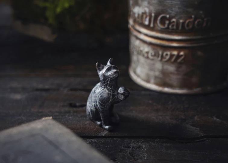 small gray cat figurine sitting on top of a table next to an old jar