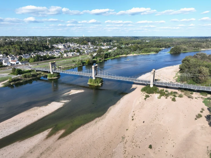 a river running past a long bridge on top of a sandy beach