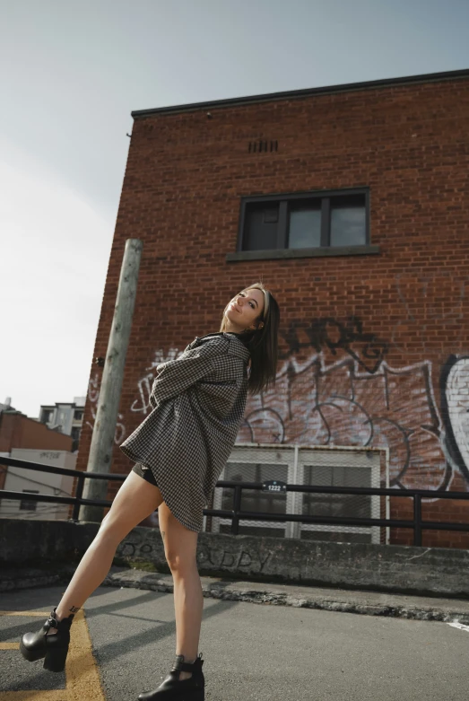 a young lady standing in front of a brick building with graffiti