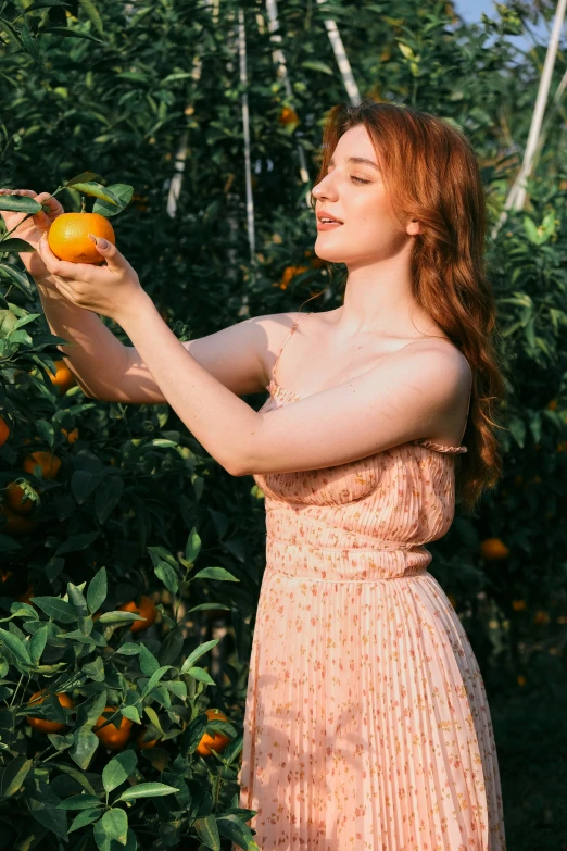 the young woman in pink dress is eating an orange