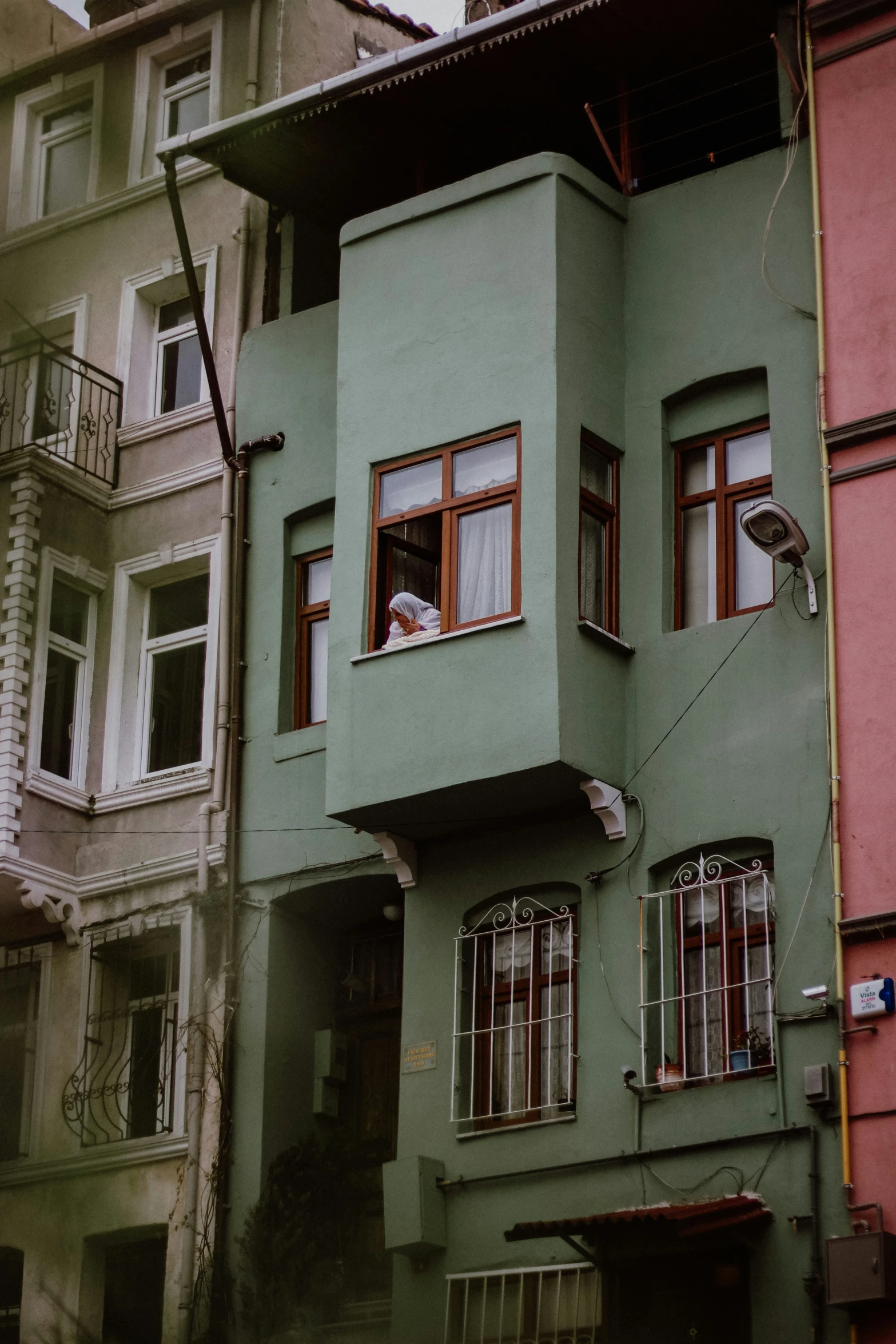 green building with two levels and two people looking out from windows