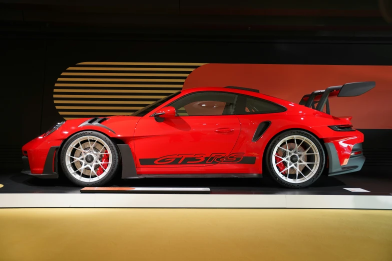 a red sports car on display in front of an orange wall