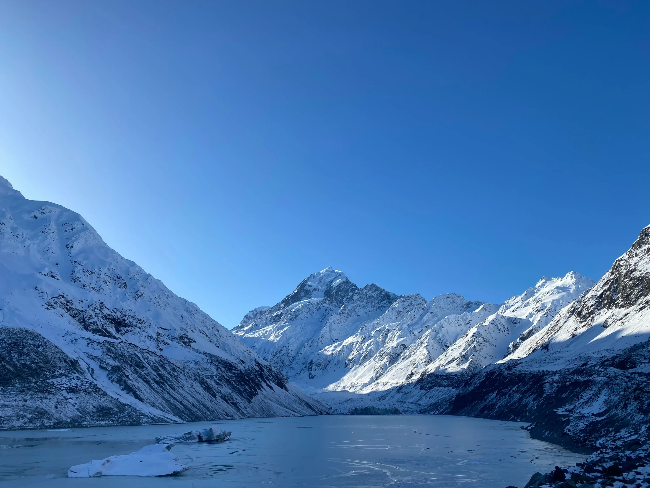 a snow covered mountain and lake under a blue sky