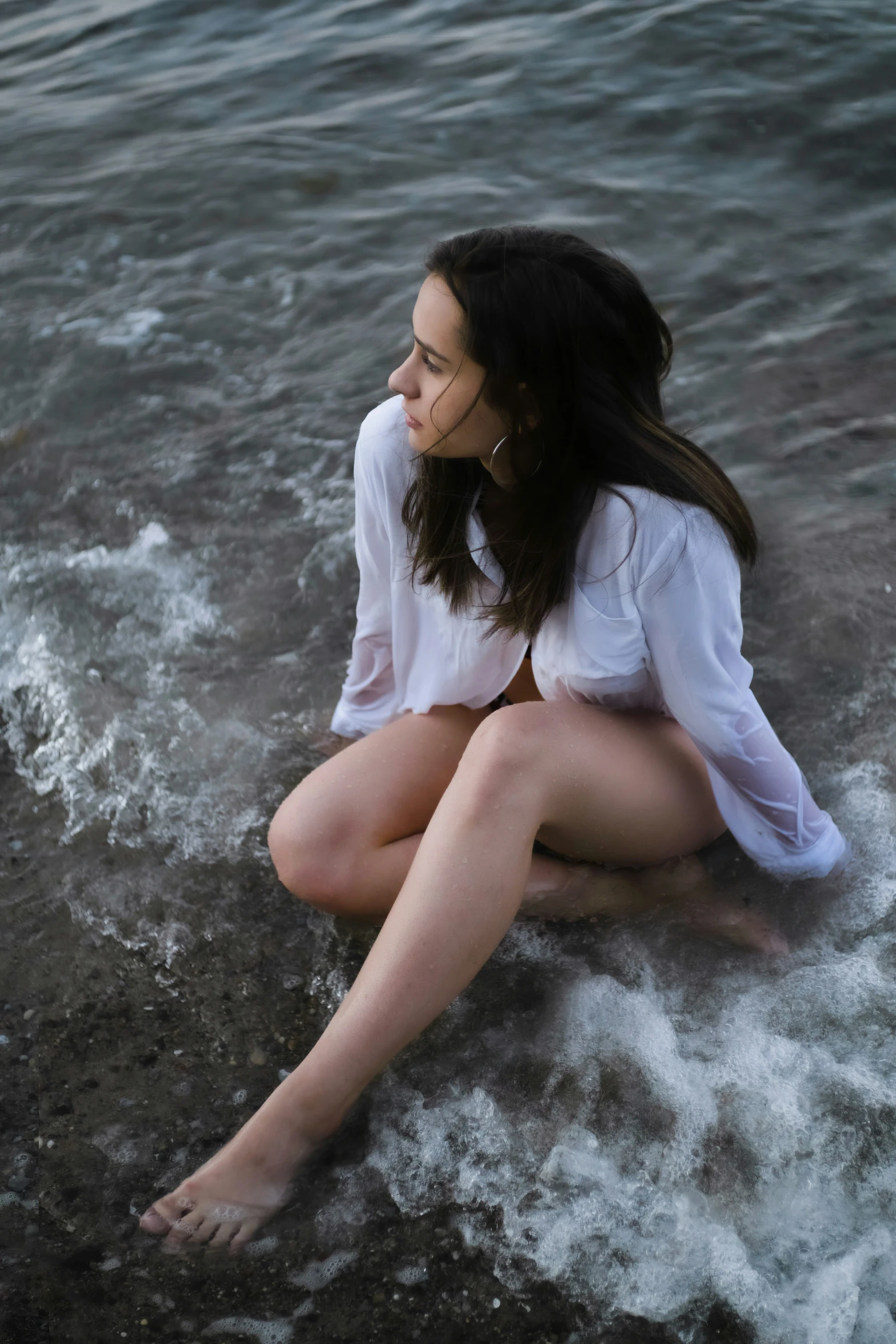 a woman with long dark hair sitting on the shore