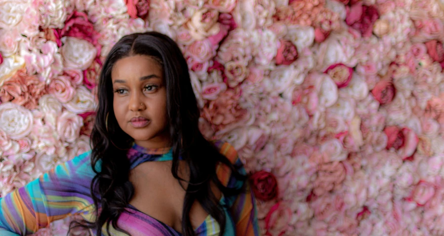 a young woman standing in front of a flower covered wall