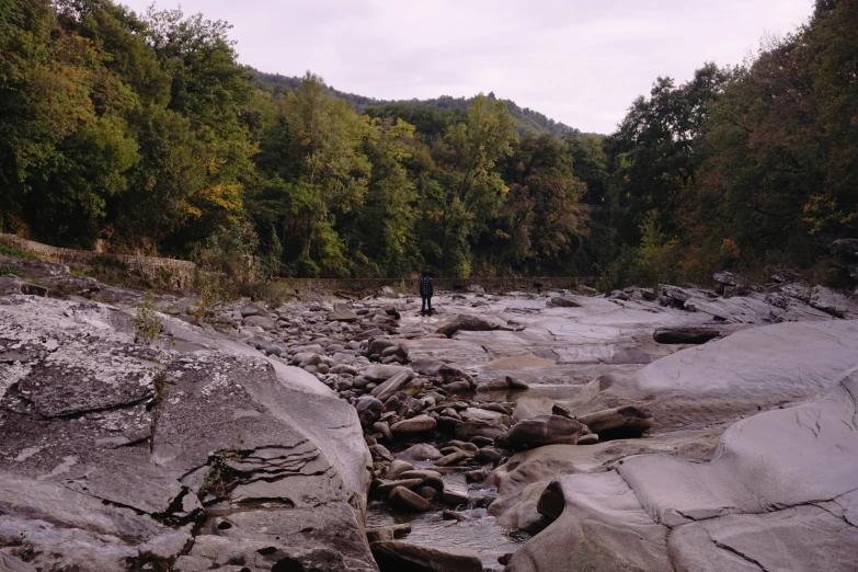 a person with an umbrella standing on rocks by a river