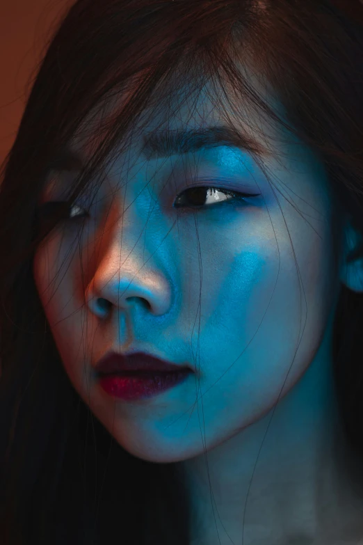 an asian woman with blue makeup and light reflecting off her face