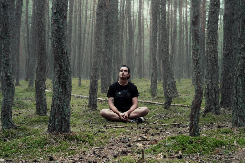 a man sitting in the middle of a forest on top of grass