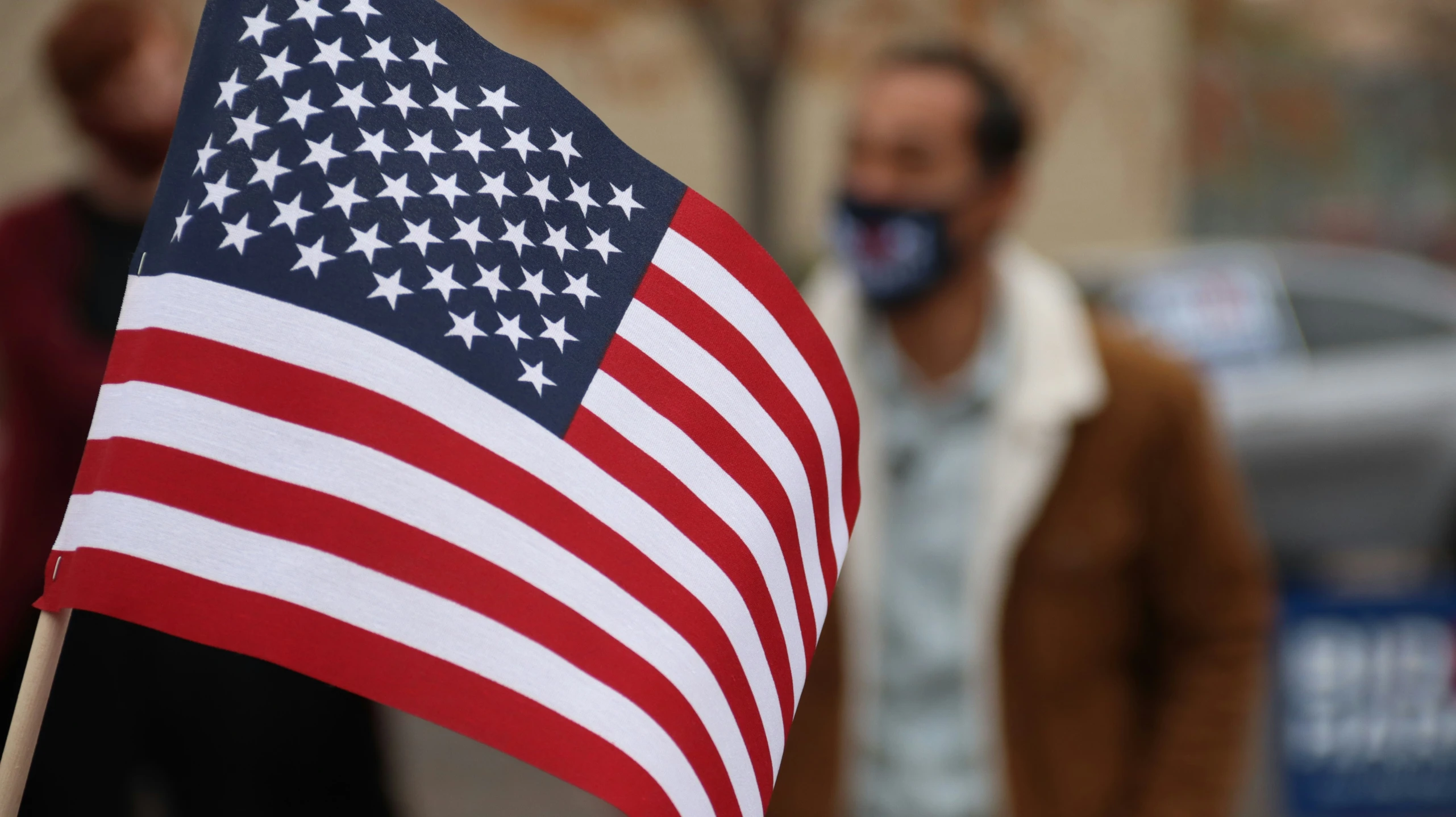 a person wearing a mask standing next to an american flag