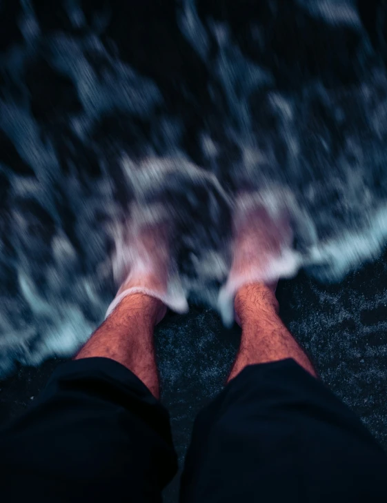 man's feet standing on the sandy beach