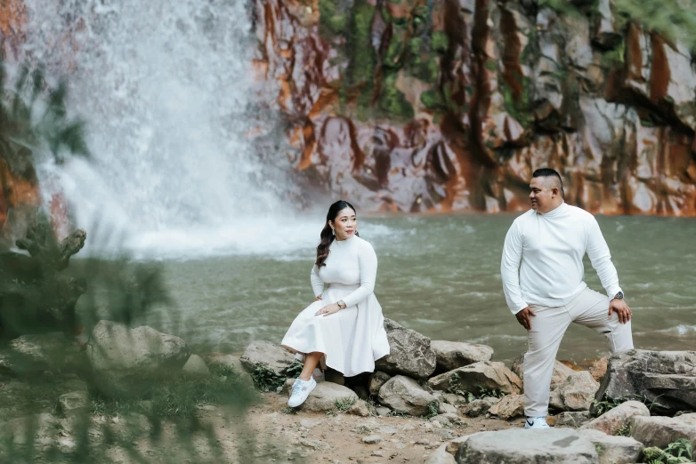 a man and woman pose in front of a waterfall