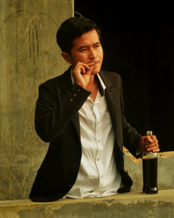 man in suit smoking cigarette sitting with a bottle and looking at the camera