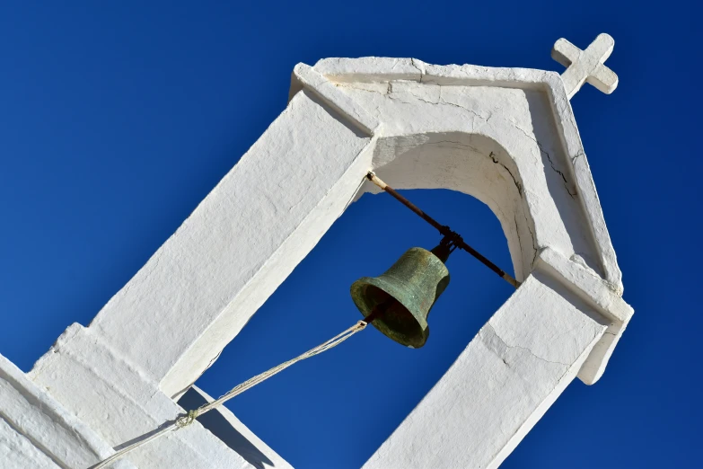 a bell with a cross hanging from it next to a white wall