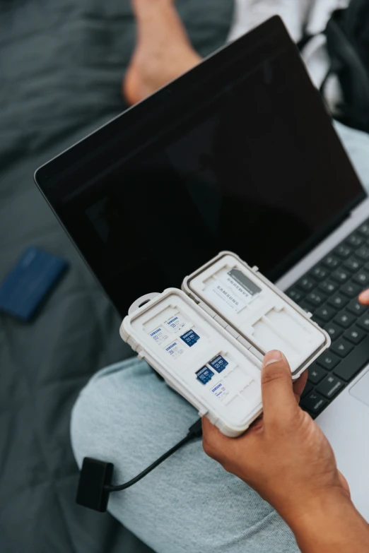 a person holds two cell phones next to a laptop computer