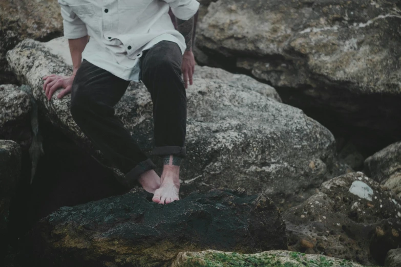 a man in white shirt sitting on rock near plants