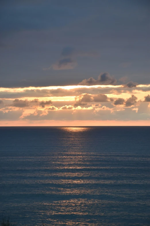 a view over the ocean to a distant sun and clouds