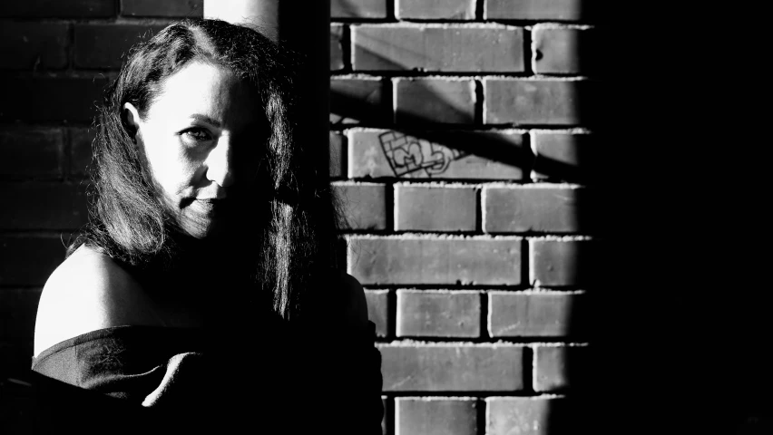 black and white po of a woman in front of a brick wall