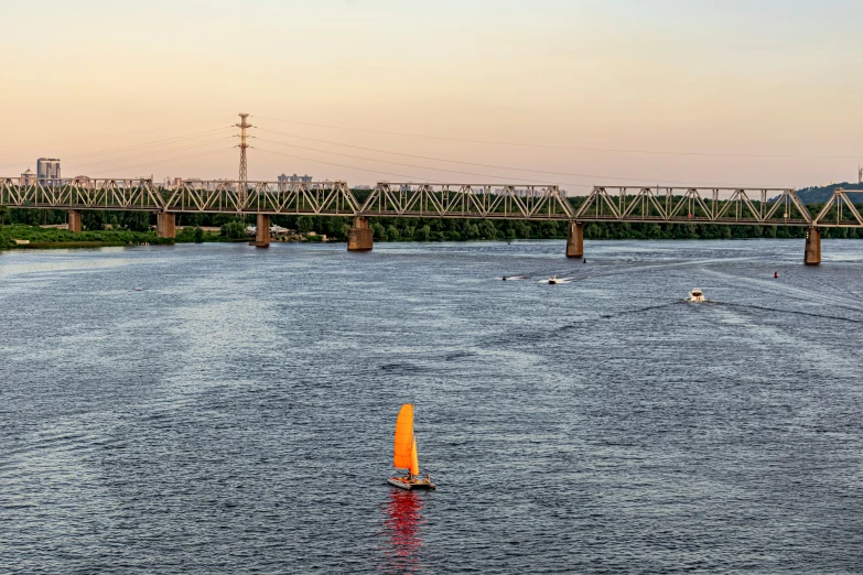 a sail boat in a river by a bridge