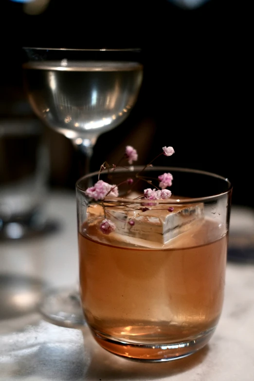 a glass of drink sits on the table with flowers growing in it