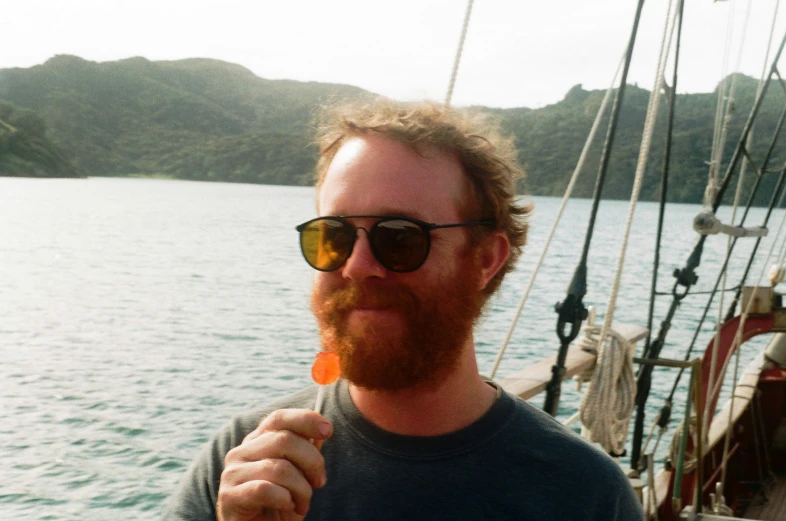 a man with red hair is eating food by the boat