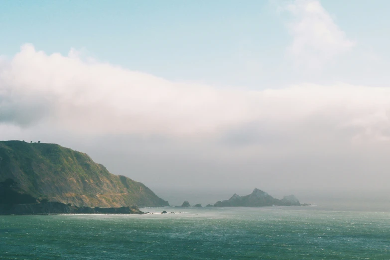 a large body of water surrounded by hills and a cloudy sky