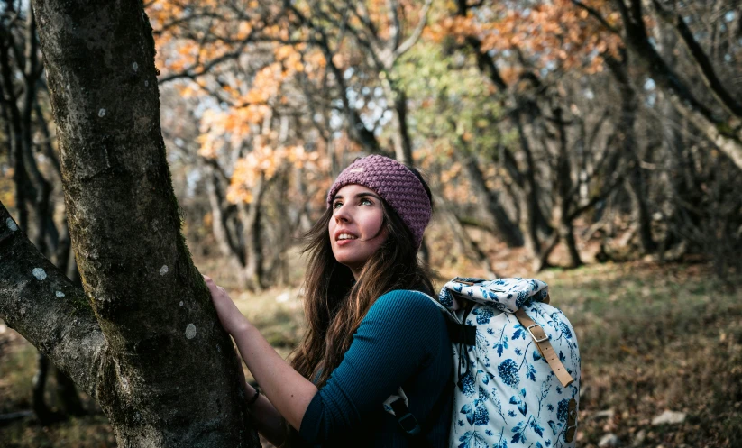 a woman in a beanie leaning on a tree in the woods