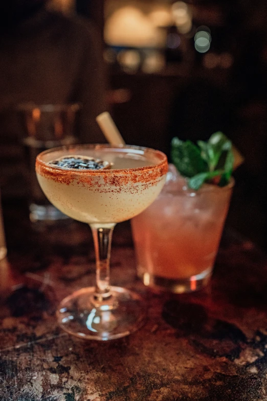 two cocktails are sitting on a bar and one is half filled with ice