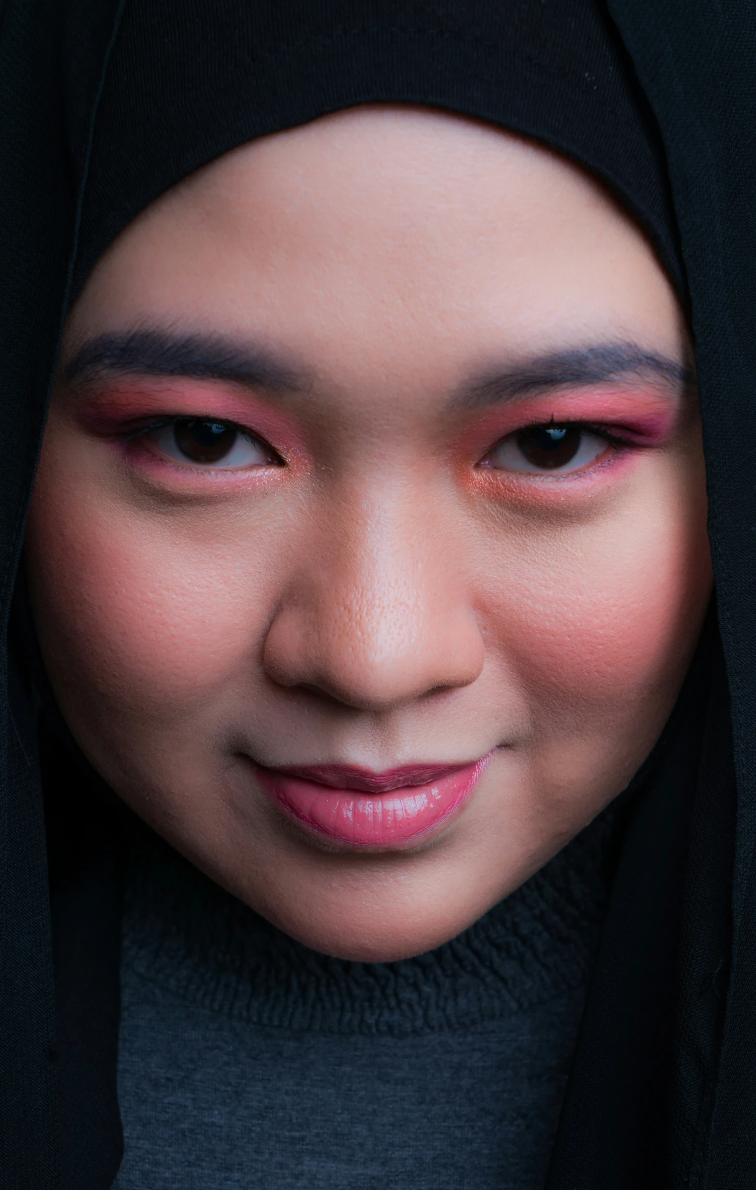 a woman in a hijab and makeup looks at the camera