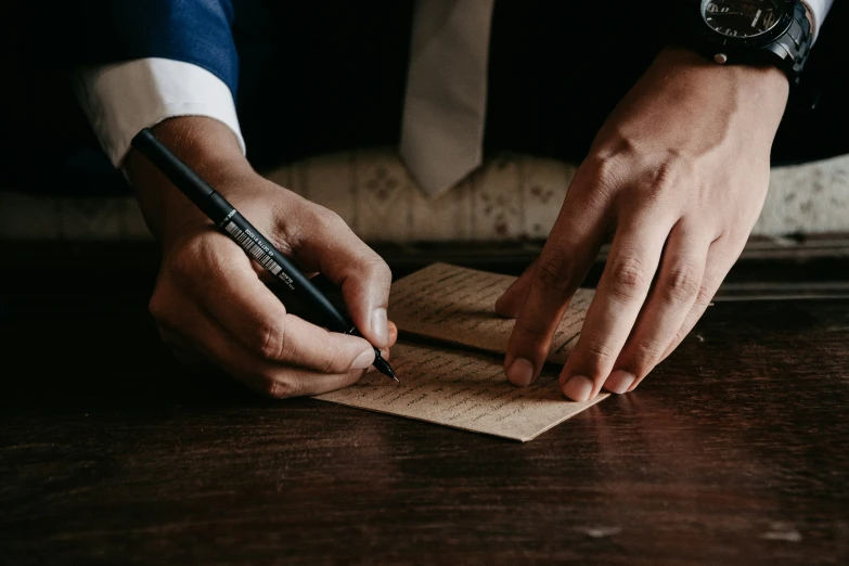 a hand writing on a piece of paper next to a pen