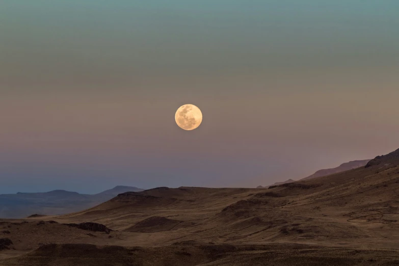 the moon is setting above a hilly area