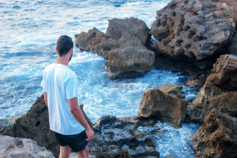 a young man standing on the edge of rocks looking at waves