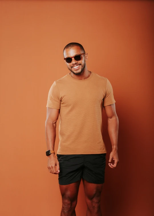 a man with short legs and a tan shirt standing in front of an orange wall