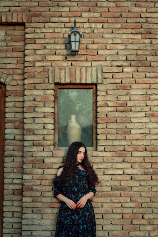 a woman is posing in front of a brick wall with a vase near by