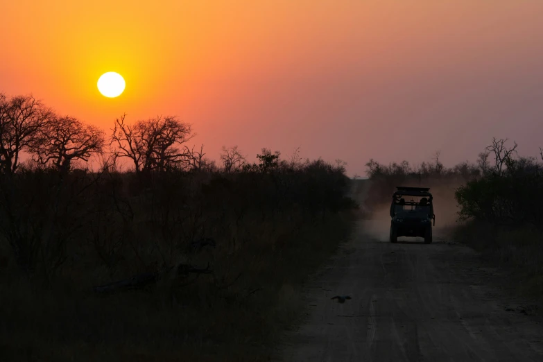 jeep driving down road toward setting sun