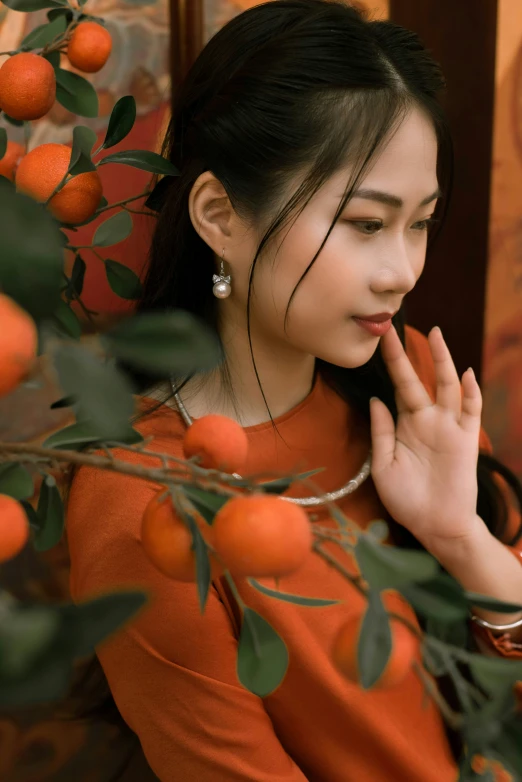 a woman with a pearl necklace and orange sweater looking down