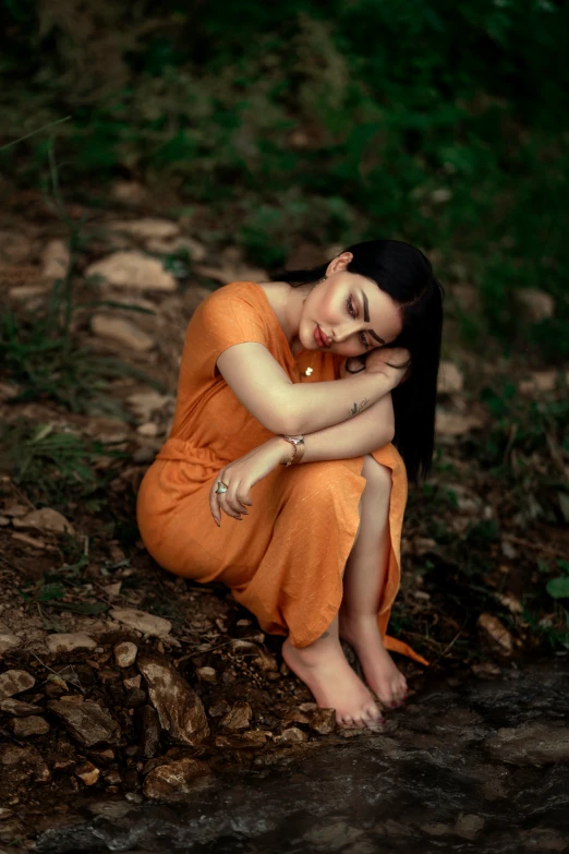 a woman in orange sitting by a stream