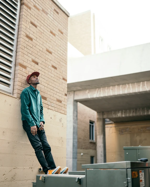 man leaning against a brick wall and wearing a green jacket