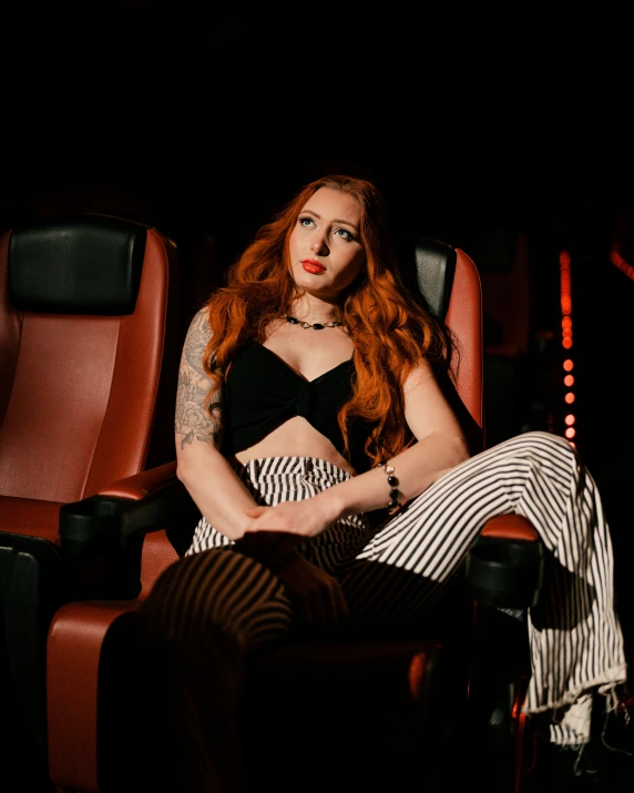 a woman is sitting in a theater with long red hair and piercings