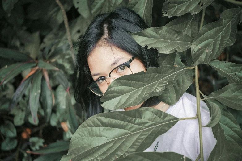 woman in glasses hiding behind nches of a tree