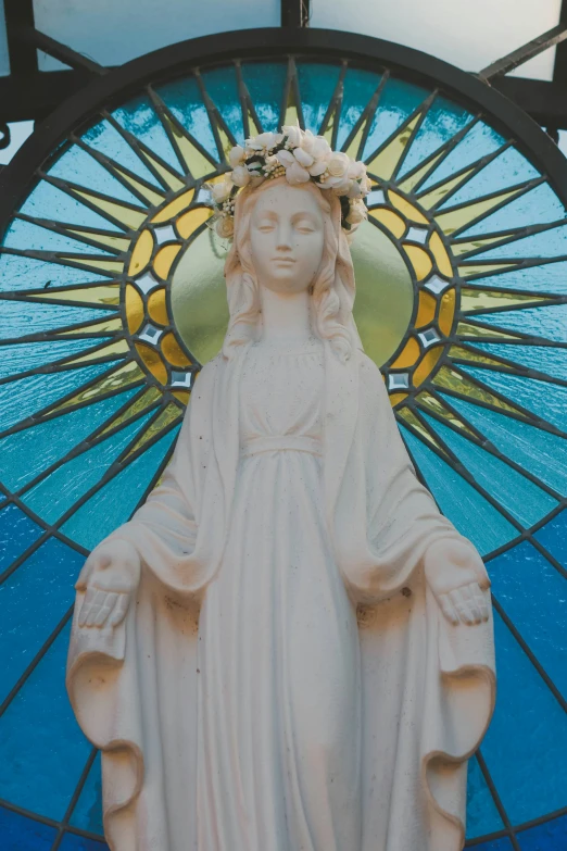 a white statue of the virgin mary with stained glass windows