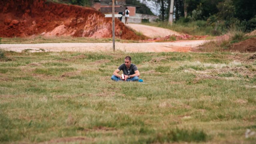 a young man sitting in the grass near the road