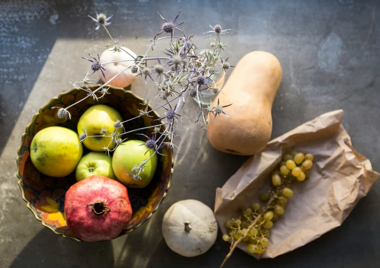 apples and pears sit in a bowl next to two potatoes