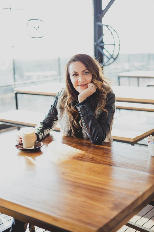 a beautiful woman sitting in front of a wooden table with a cup