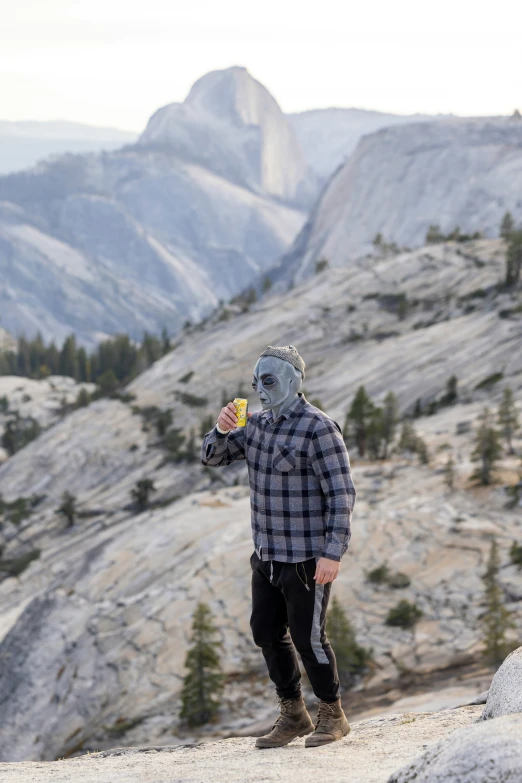 man drinking a beverage on top of a mountain in the wilderness