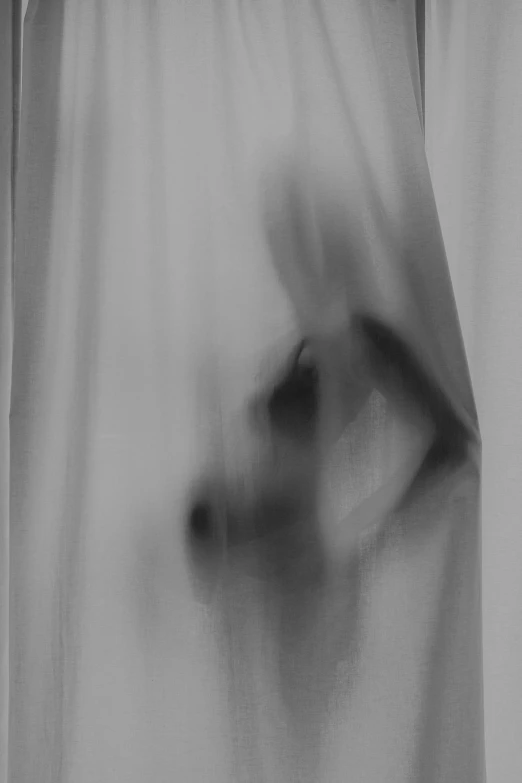 blurred black and white pograph of a person looking through a curtain