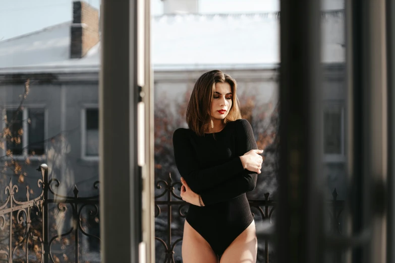 a woman in black bodysuit leaning against a fence