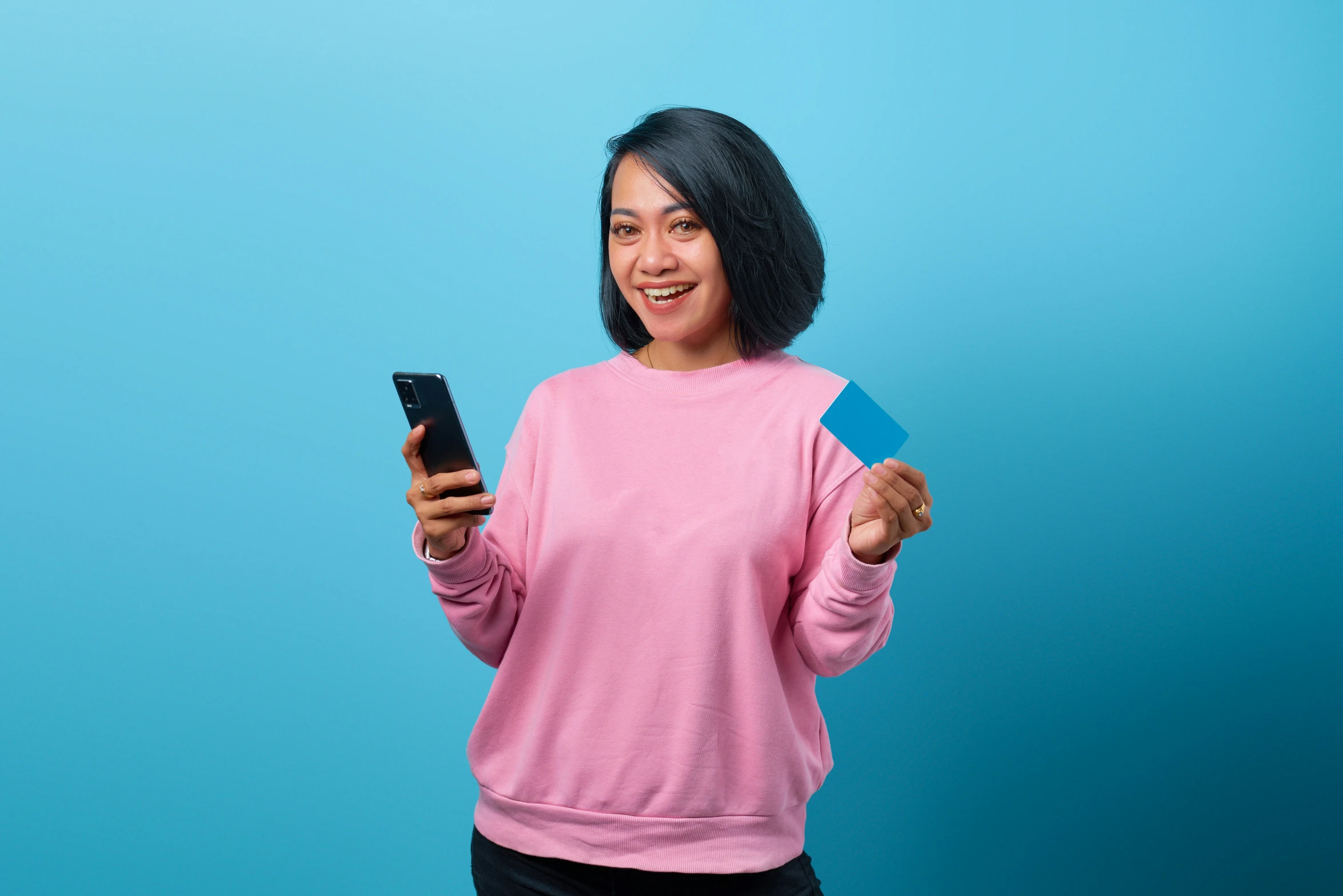 woman in pink sweater holding a credit card and cell phone