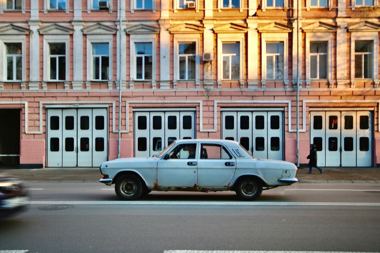 a white car driving past a pink building on the road